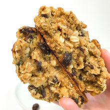 Load image into Gallery viewer, holding an open oatmeal raisin pudge showing a gooey center with plump raisins and toasted oats
