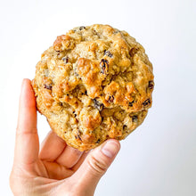 Load image into Gallery viewer, holding a single oatmeal raisin pudges in all its golden glory. some raisins showing through
